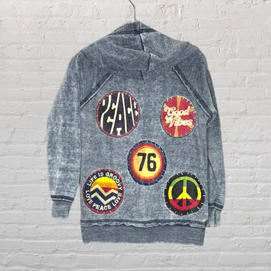 Grey hoodie featuring various retro multicolored patches with messages like 'Peace', 'Good Vibes', and 'Life is Groovy'.