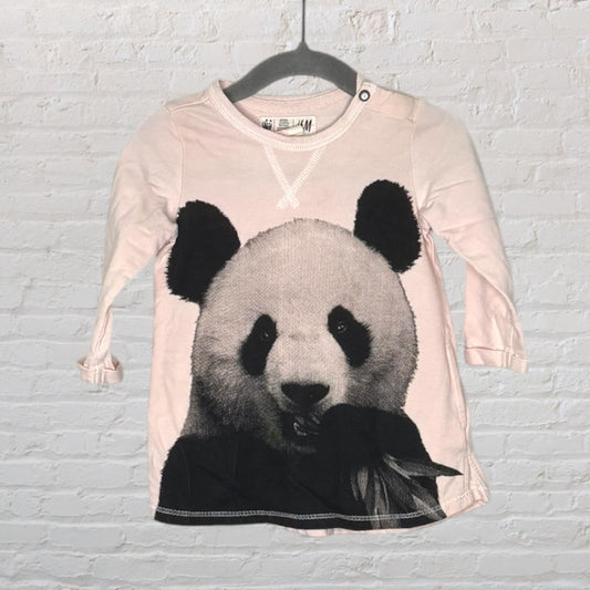 Light pink long sleeve top with a large panda print, featuring a button detail on the shoulder, hanging on a black hanger.