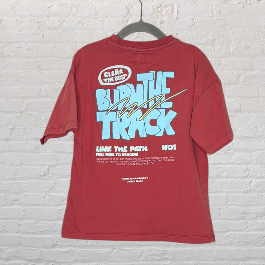 Red T-shirt with large blue and white text graphic 'Burn the Track' and motivational phrases, hanging on a hanger.