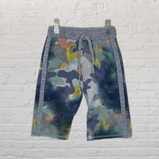 Camouflage print shorts with a drawstring waistband, displayed against a white brick wall.