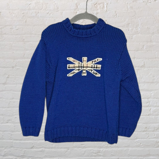 Blue knit sweater featuring a plaid Union Flag motif on the front, hanging on a hanger against a brick wall.