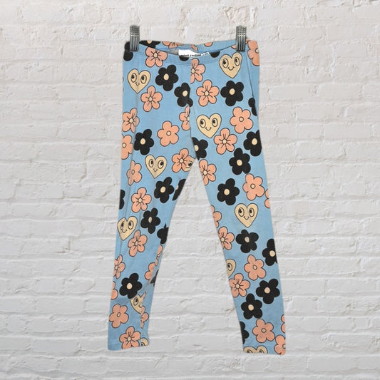Colorful leggings with a floral and heart pattern on a blue background, hanging on a white brick wall.