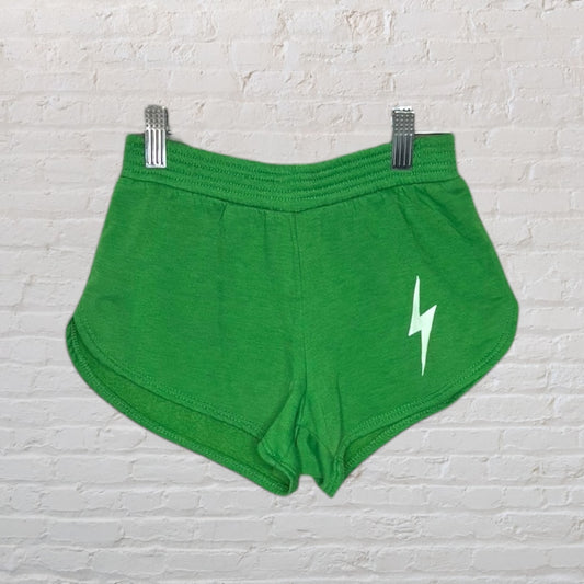 Bright green athletic shorts with a white lightning bolt design on the front, hanging on a white brick background.