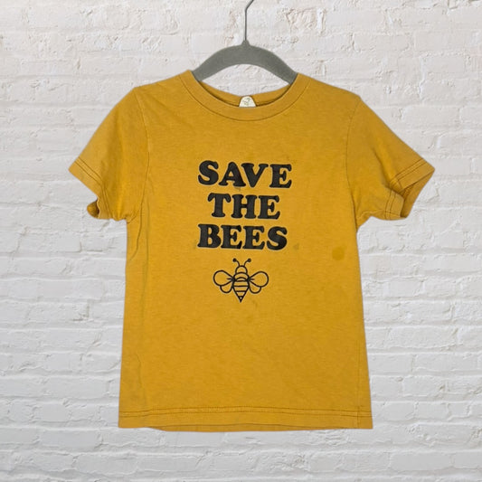 Mustard yellow T-shirt with 'Save The Bees' text and bee graphic, hanging on a hanger.
