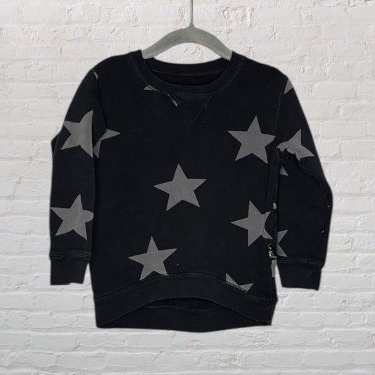 Black sweatshirt with grey star patterns displayed on a hanger against a white brick wall.