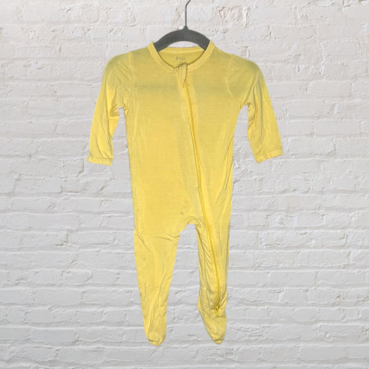 Yellow baby footed sleeper with long sleeves and a front zipper, hanging on a black hanger against a white brick wall.