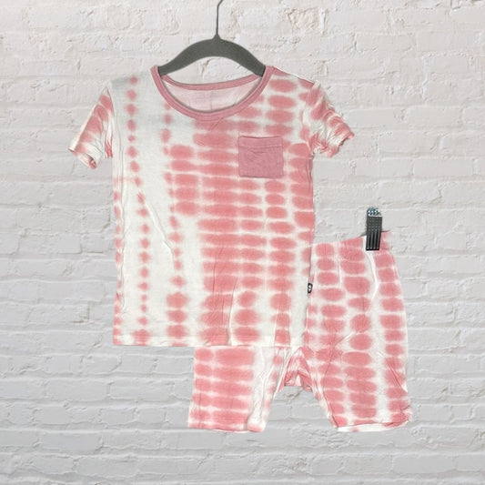 Pink and white tie-dye pajama set with short sleeves and a pocket, hanging against a white brick wall.