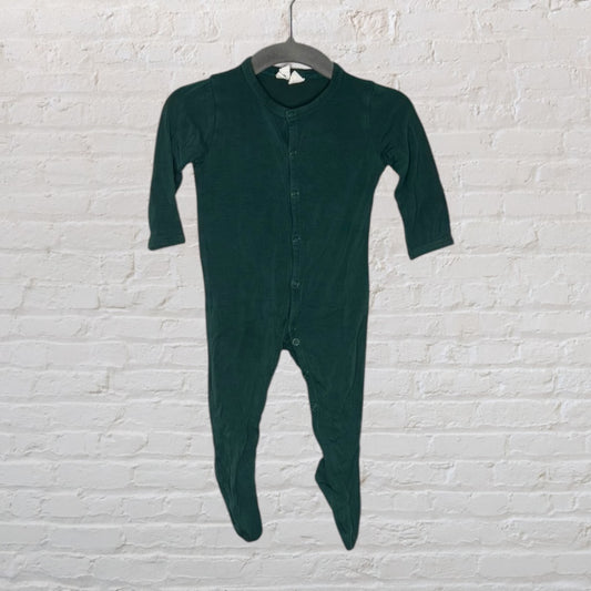 Forest green footed baby onesie with long sleeves and a front button closure, hanging on a hanger against a white brick wall.