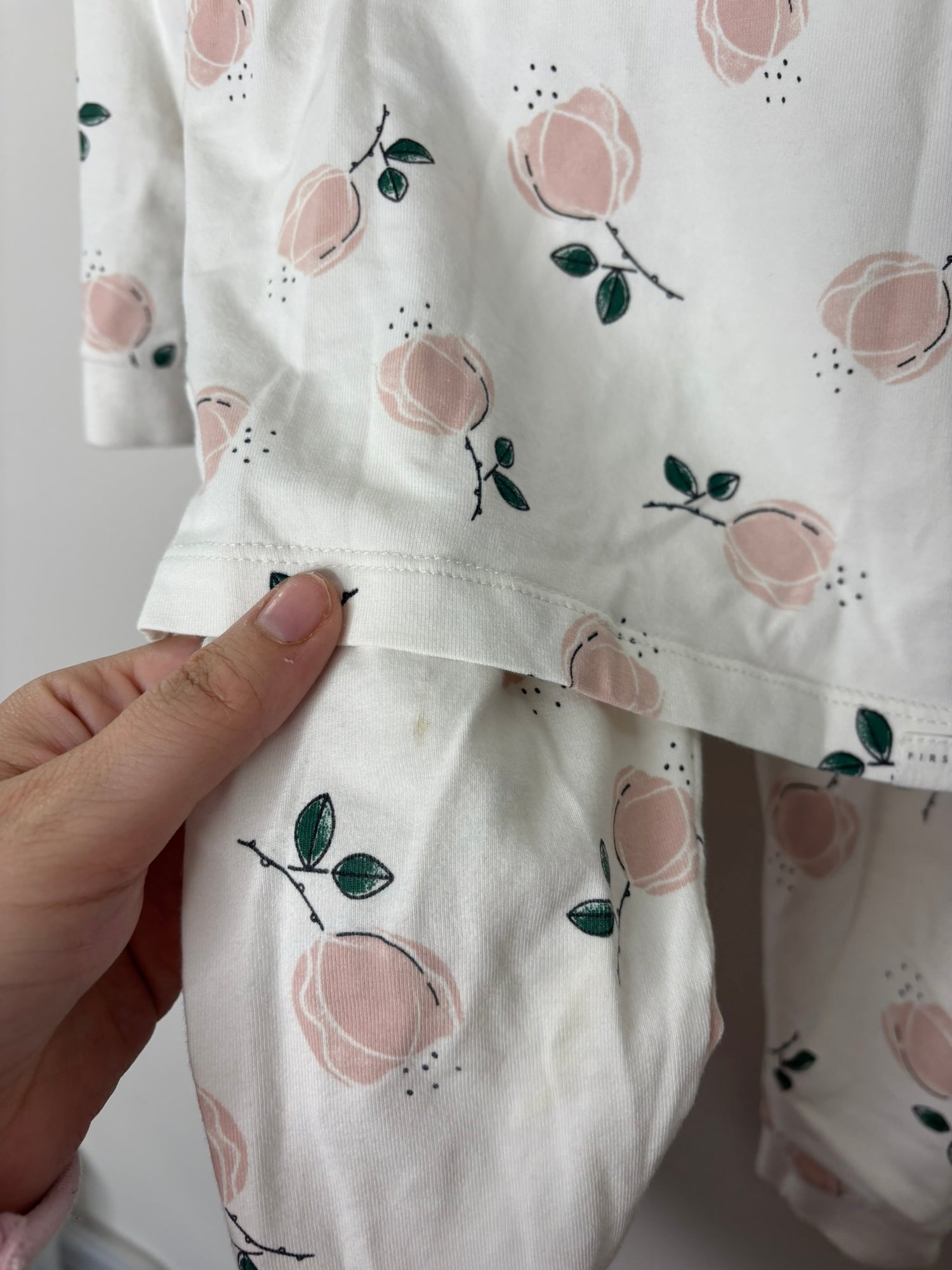 White pajama set with peach and green leaf patterns, featuring a top and bottom hanging on a gray hanger.