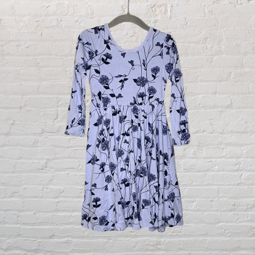 Light blue long sleeve dress with dark floral print, hanging on a white brick wall.