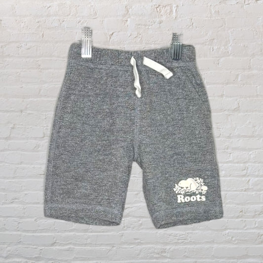 Grey knit shorts with a drawstring and Roots logo, featuring a beaver design, displayed against a brick wall.
