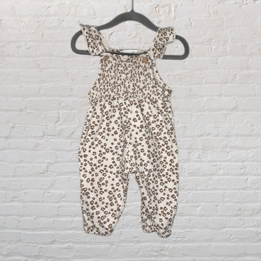 Cream baby romper with brown floral print, featuring smocked details and buttoned straps, hanging on a hanger.