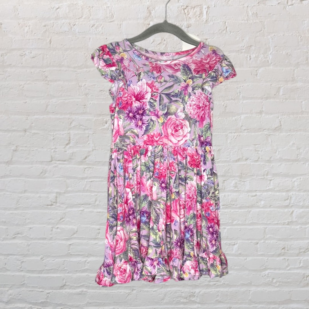 Pink and purple floral print dress with cap sleeves and ruffle hem, hanging on a hanger against a white brick wall.