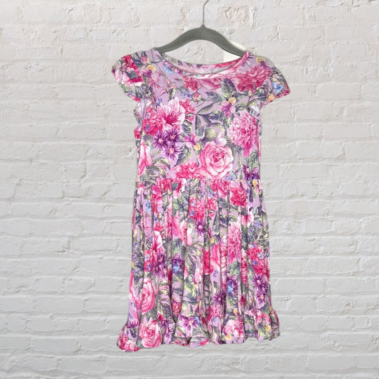 Pink and purple floral print dress with cap sleeves and ruffle hem, hanging on a hanger against a white brick wall.