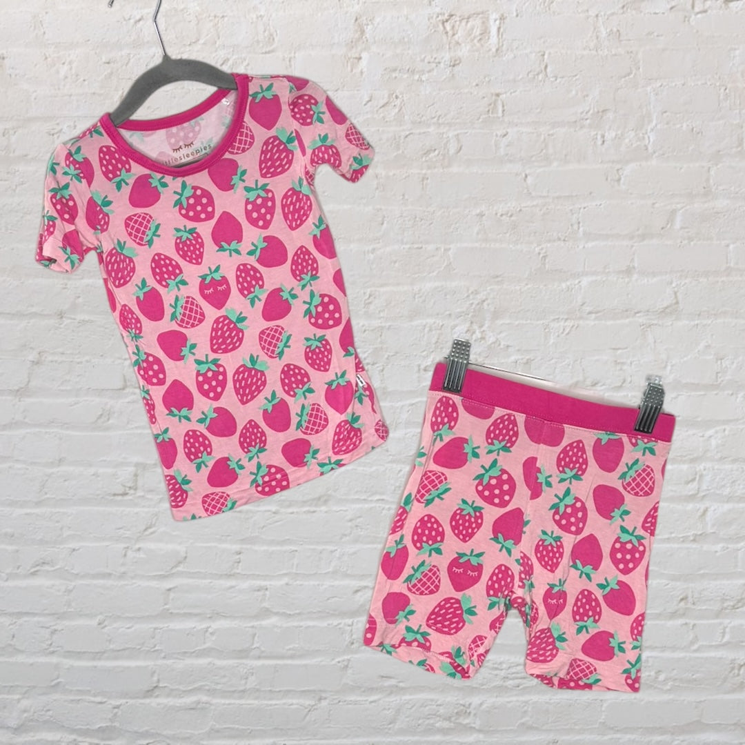 Pink sleepwear set with a strawberry pattern, consisting of a short-sleeve top and matching shorts, displayed on hangers against a white brick wall.