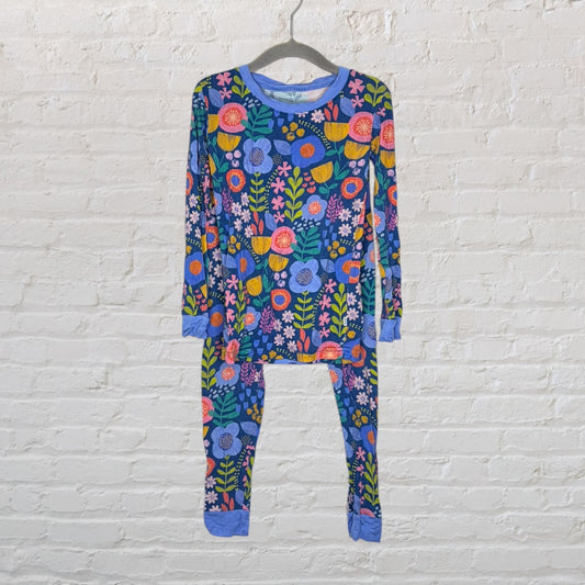 Colorful floral patterned pajama set with a blue base, featuring long sleeves and pants, displayed on a hanger against a white brick wall.