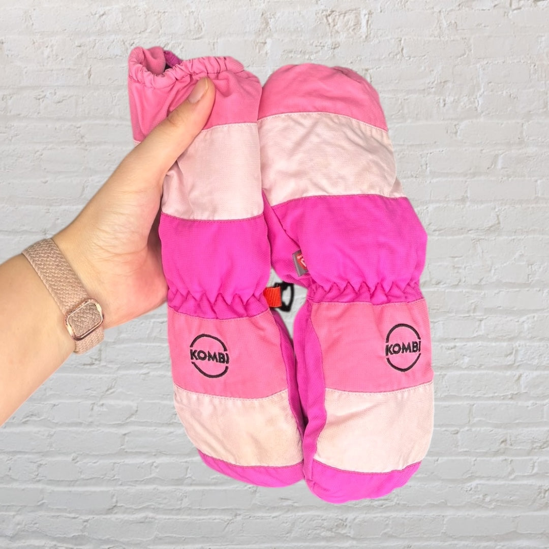 Kombi mittens in various shades of pink with logo, held by a hand against a brick background.