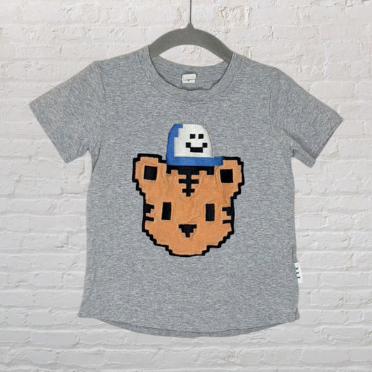 Gray t-shirt with a pixelated tiger face wearing a blue and white cap, hanging on a hanger.