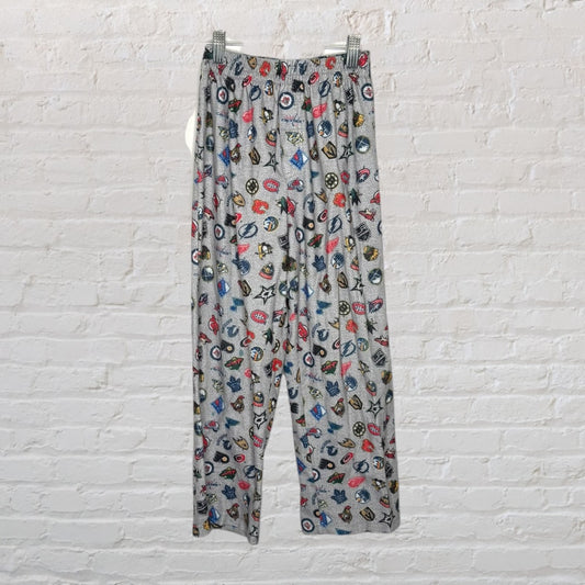 Grey lounge pants with a colorful all-over graphic print, displayed against a white brick wall.