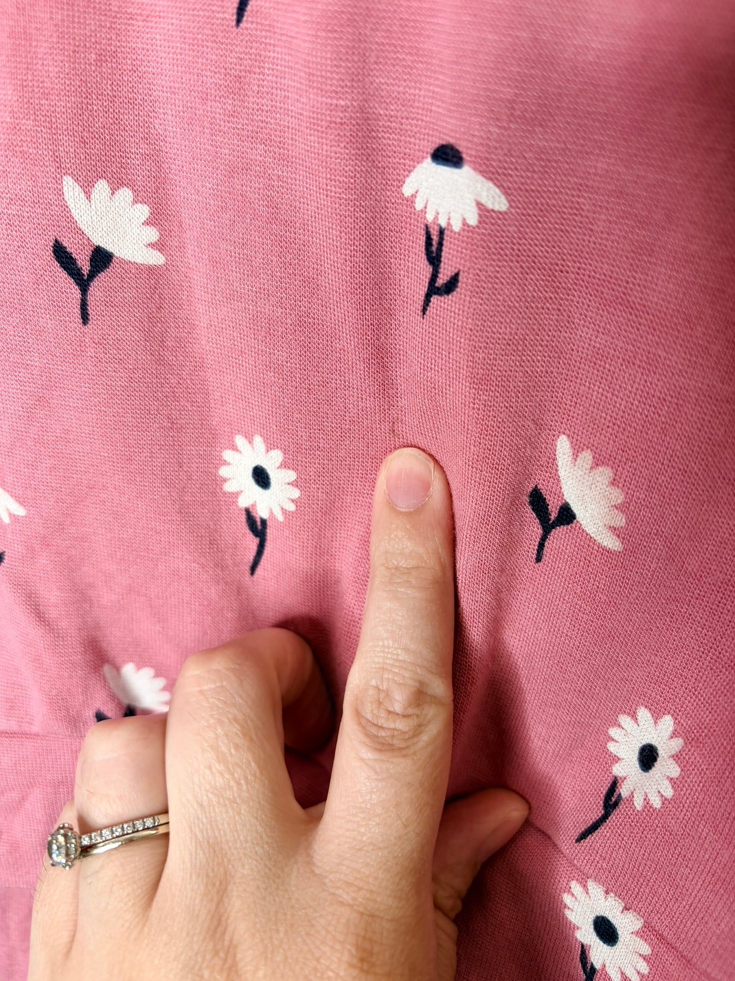 Pink pajama set with white floral design on a hanger against a white brick wall.