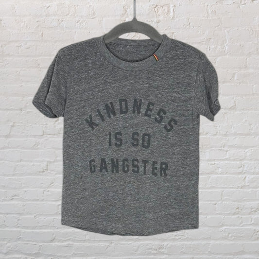 Heather gray T-shirt with 'Kindness Is So Gangster' text, displayed on a hanger against a white brick wall.