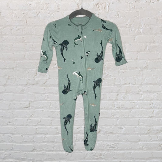 Seafoam green baby onepiece pajama with shark print, hanging on a hanger against a white brick wall.