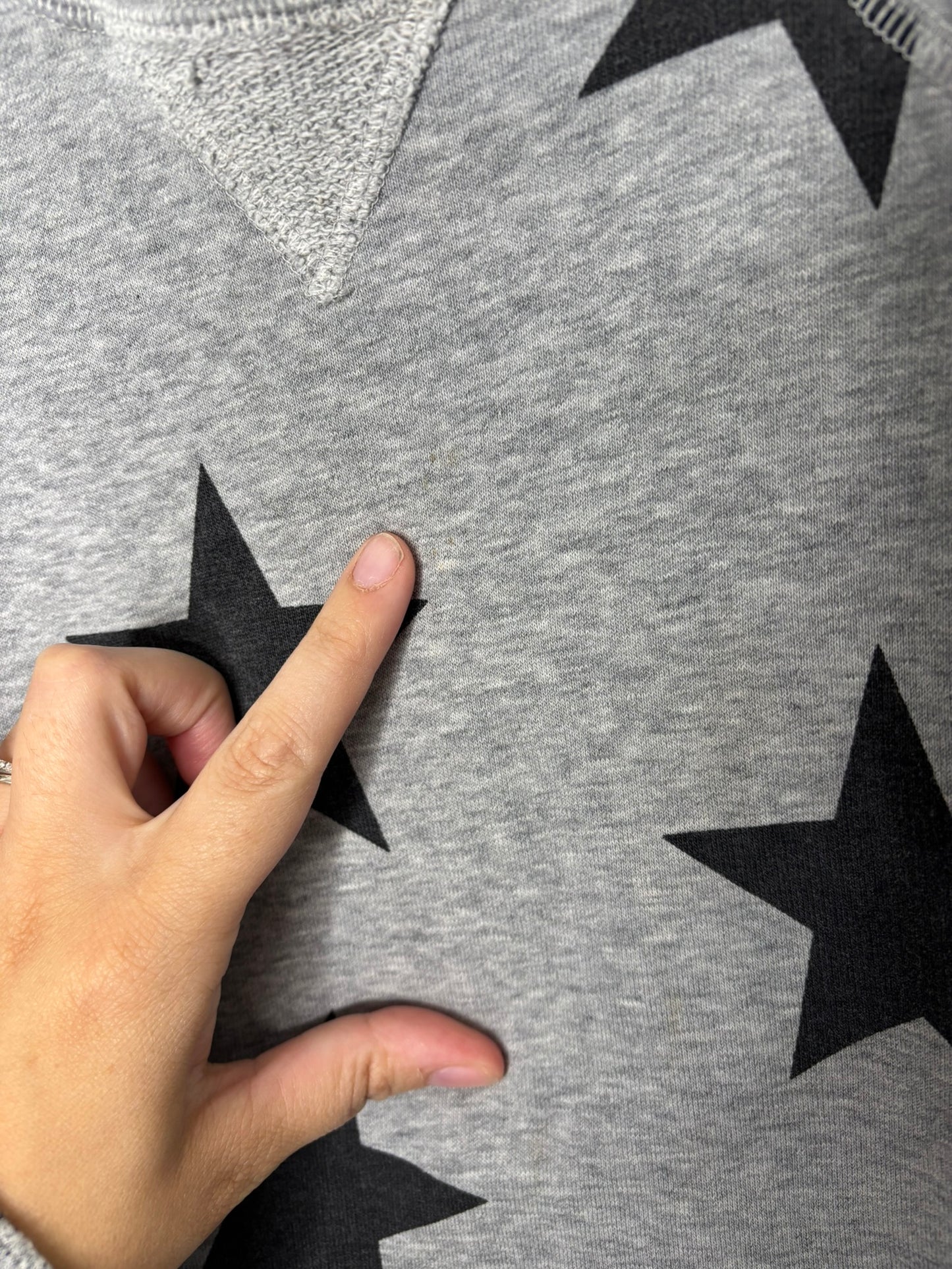 Grey sweatshirt with black star patterns, displayed on a hanger against a white brick wall.