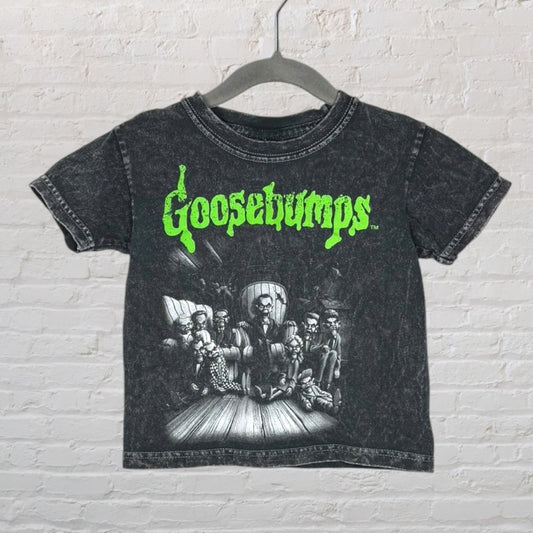Black vintage-style tee with neon green Goosebumps logo and a spooky graphic, hung on a hanger.