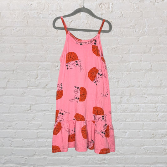 Cute pink sundress with playful orange cartoon print, featuring spaghetti straps and ruffled hem, on a hanger.