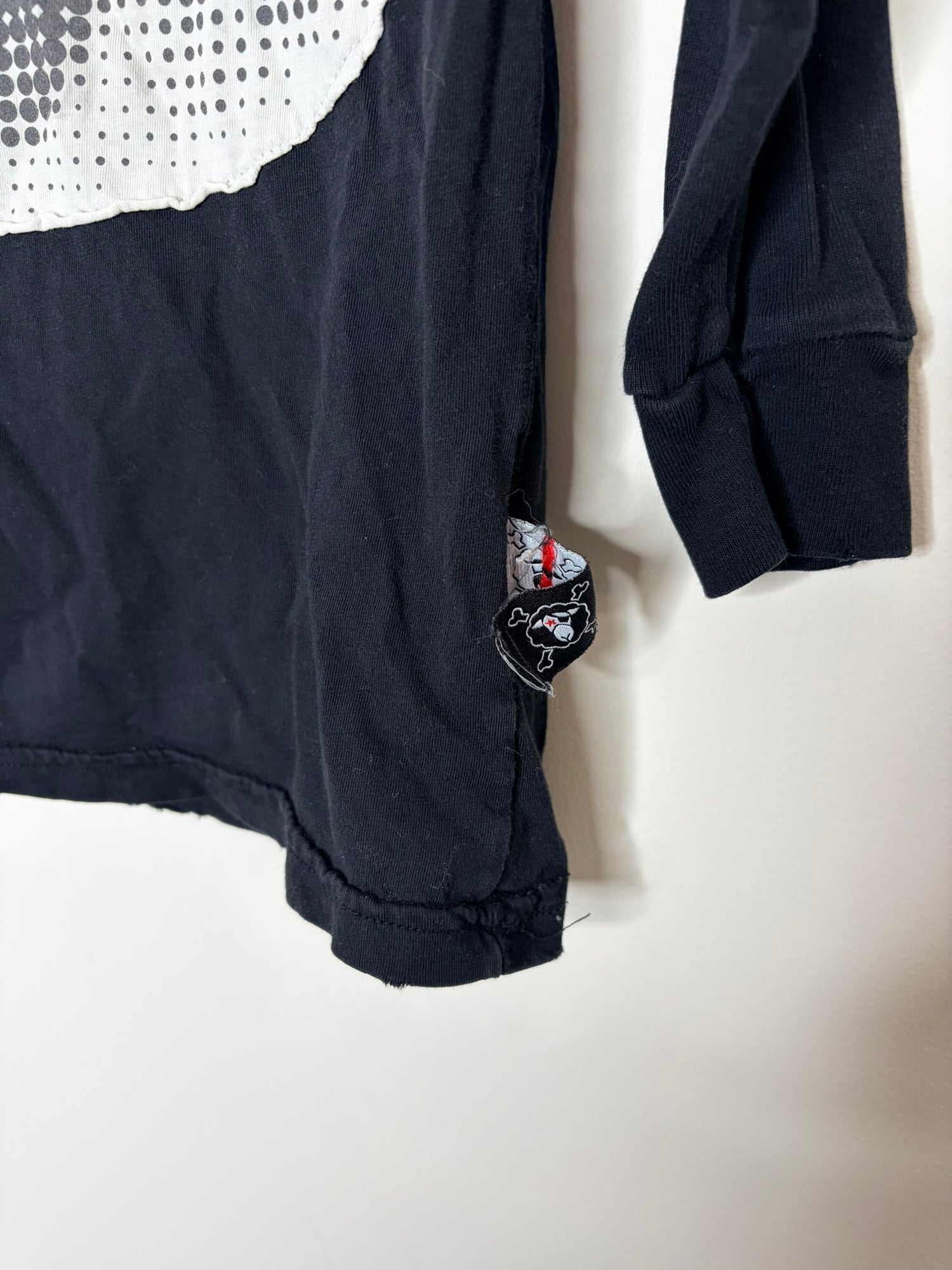 Black long sleeve t-shirt with a large white graphic eye design on the front, hanging against a brick wall backdrop.