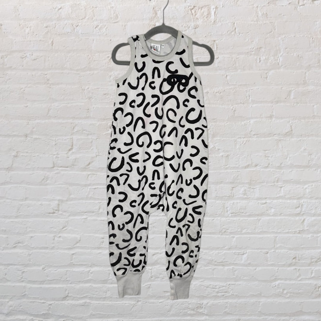 A sleeveless jumpsuit with black leopard print on a white background hanging against a white brick wall.