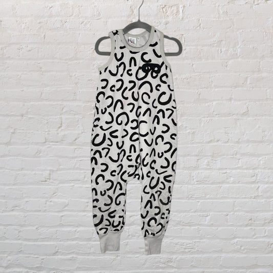 A sleeveless jumpsuit with black leopard print on a white background hanging against a white brick wall.