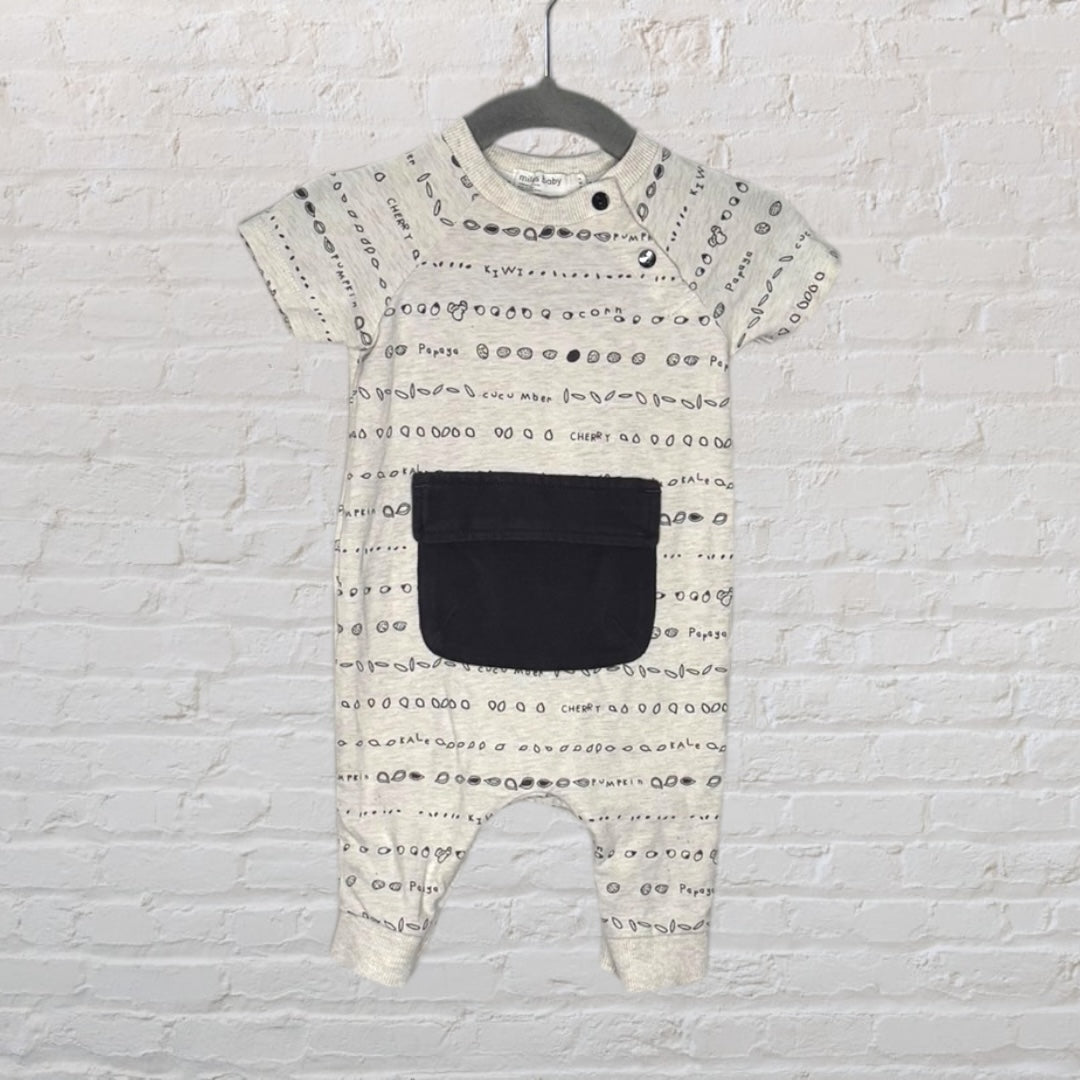 Cream-colored baby jumpsuit with black print and a large front pocket, displayed on a hanger.