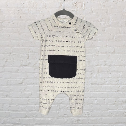 Cream-colored baby jumpsuit with black print and a large front pocket, displayed on a hanger.