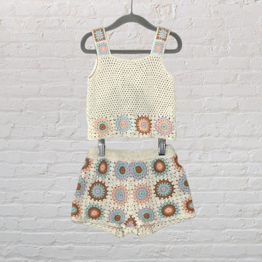 Cream crochet top and shorts set with multicoloured circular patterns hanging on a hanger against a brick wall.