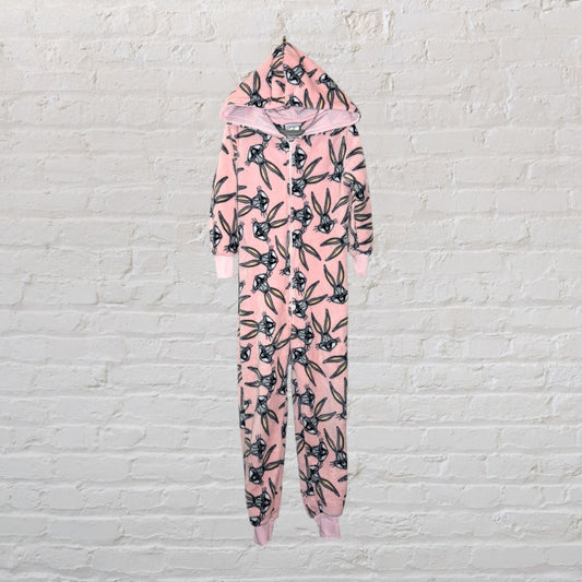 Pink onesie with Bugs Bunny graphic print and hood, hanging against a brick wall.