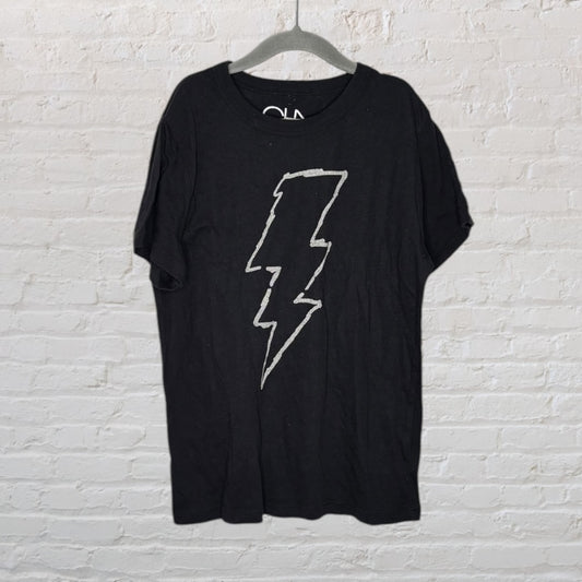 Black T-shirt with a white lightning bolt graphic, hanging on a hanger against a white brick wall.