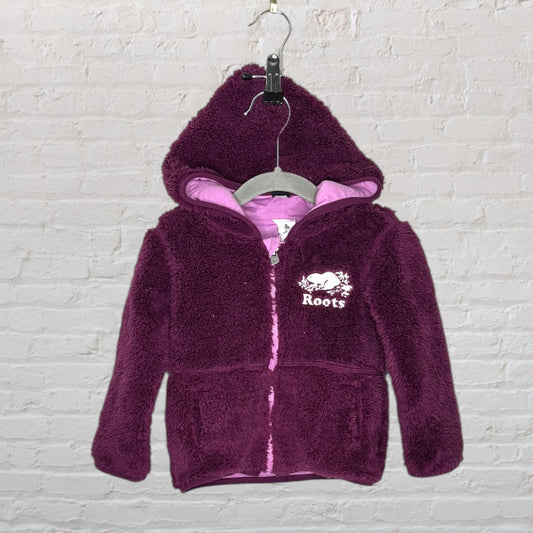 Plum fleece hoodie with pink lining and Roots logo, zip-up front, hanging on a hanger against a brick wall.