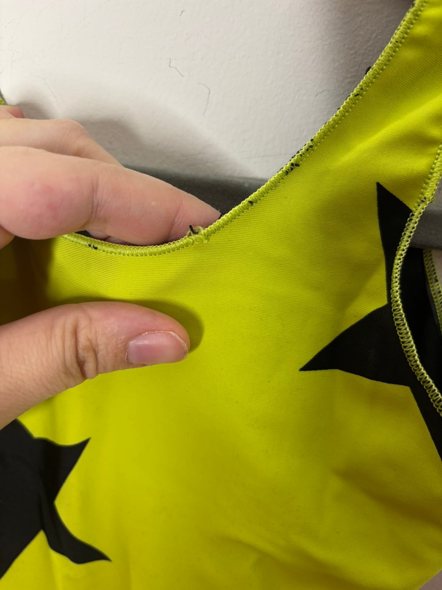 Neon yellow one-piece swimsuit with black star prints, hanging on a hanger against a white brick wall.