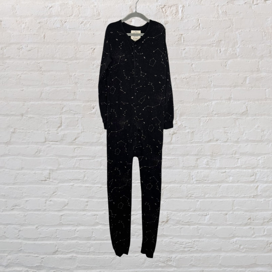 Black onesie sleepwear with constellation pattern, hanging against a white brick wall.