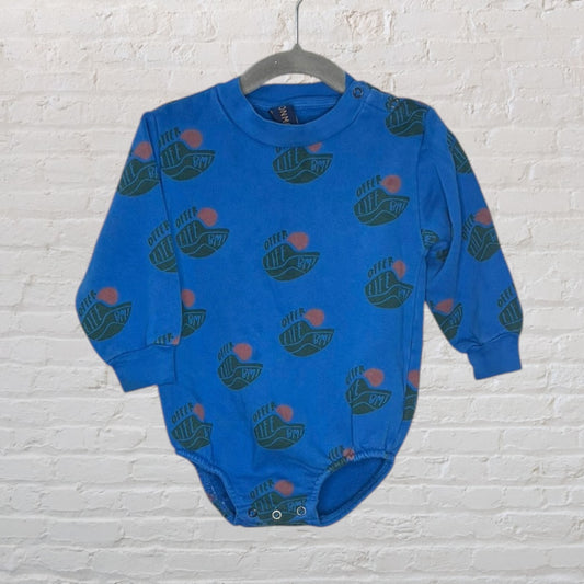 Blue baby bodysuit with long sleeves and graphic print, featuring snap buttons at the shoulder and bottom for easy dressing, hanging on a hanger against a white brick wall.