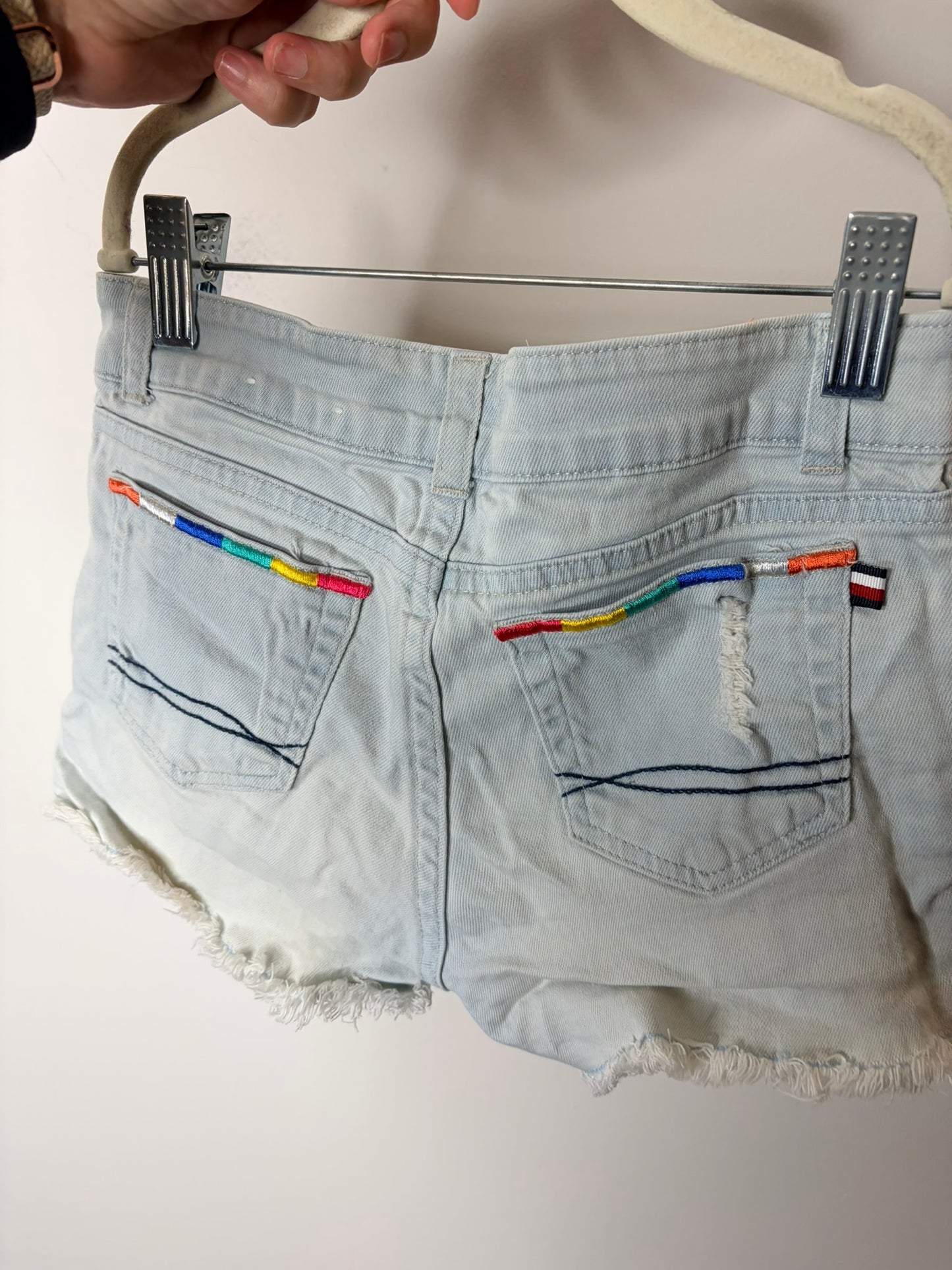 Light blue denim shorts with colorful embroidery on the pockets and frayed hem, displayed against a white background.