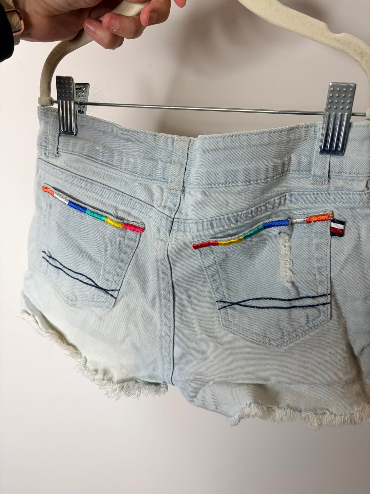 Light blue denim shorts with colorful embroidery on the pockets and frayed hem, displayed against a white background.