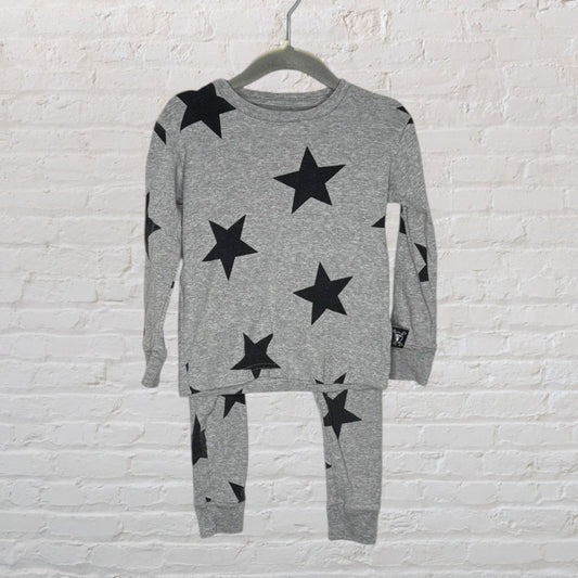 Gray pajama set with black star patterns, long sleeves and pants, hanging on a hanger against a brick wall.