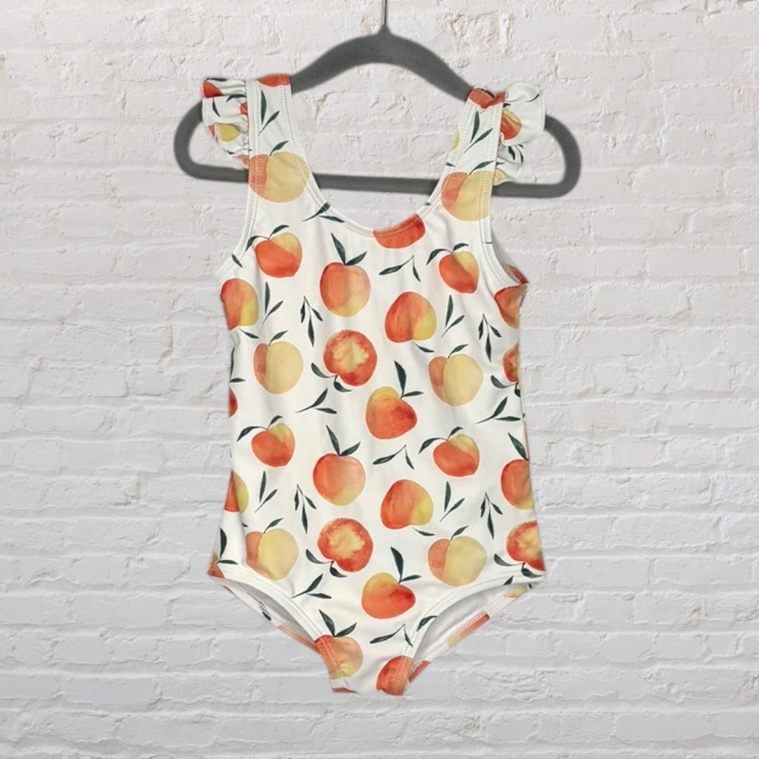 White swimsuit with peach pattern and ruffle straps hanging on a black hanger.