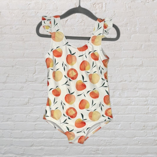White swimsuit with peach pattern and ruffle straps hanging on a black hanger.