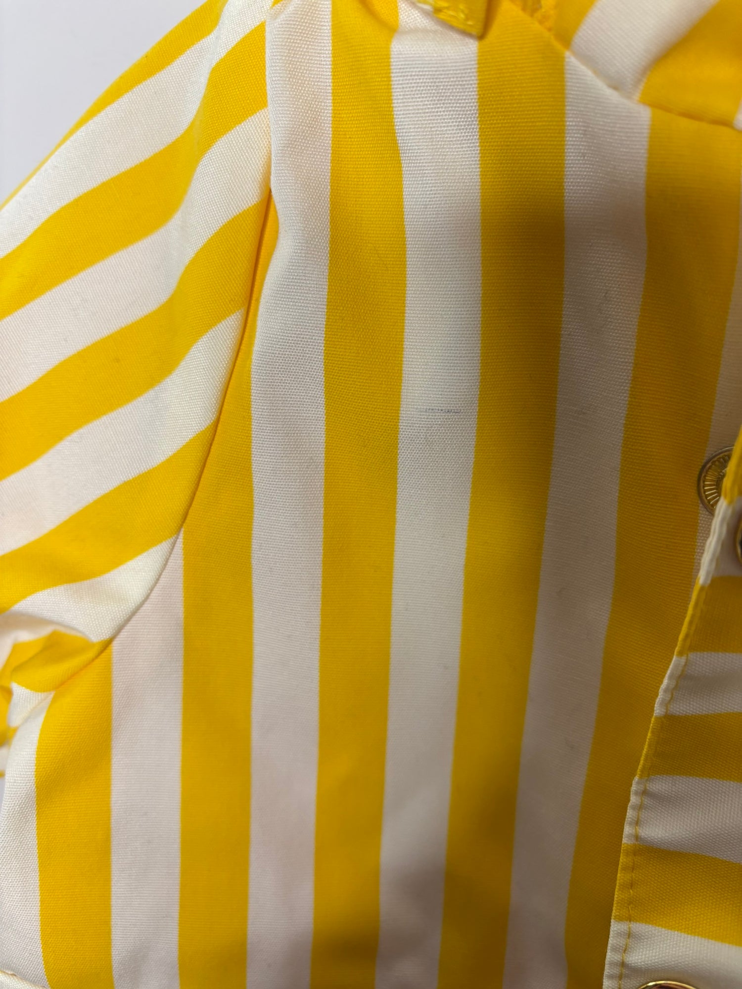 Yellow and white striped hooded raincoat for kids, featuring buttons and front pockets, hanging against a brick wall.