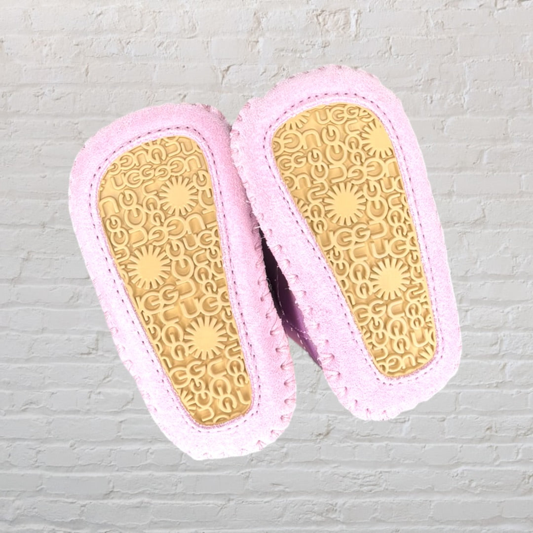 Pair of metallic pink baby booties with soft faux fur lining, held by a hand.