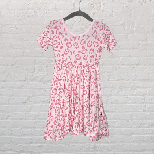 A pink leopard print dress on a hanger against a white brick wall.