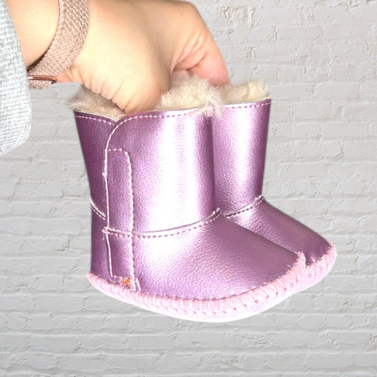 Pair of metallic pink baby booties with soft faux fur lining, held by a hand.
